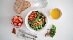 Top view of a healthy salad and fresh ingredients with bread and juice on a white surface.