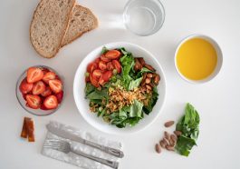 Top view of a healthy salad and fresh ingredients with bread and juice on a white surface.